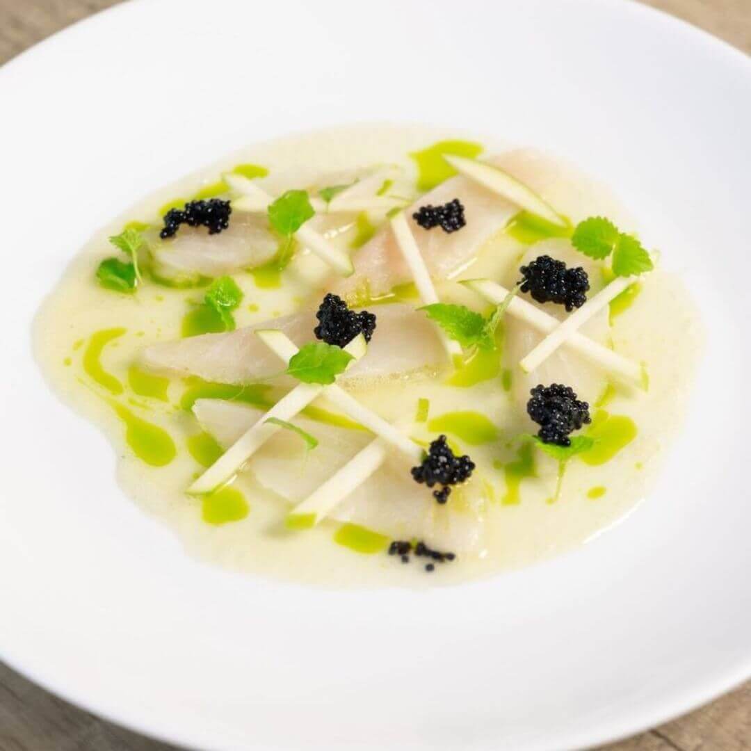 A vibrant dish with pieces of kingfish and apple and lime slices